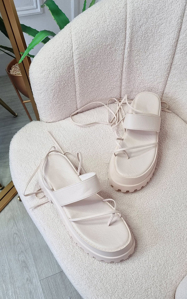 Faux Leather Strappy Lace Up Sandals elegantly draped on a chair, showcasing stylish faux leather construction with statement straps and secure lace-up ankle design.