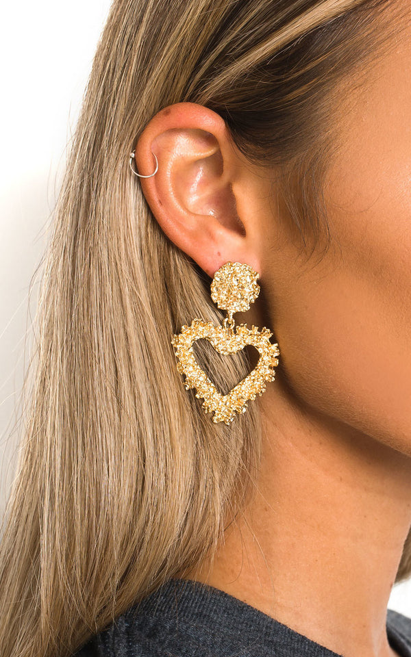 Close-up of a woman's ear adorned with NASCERA Statement Heart Earrings, showcasing a retro heart design with a raised effect and post backings.