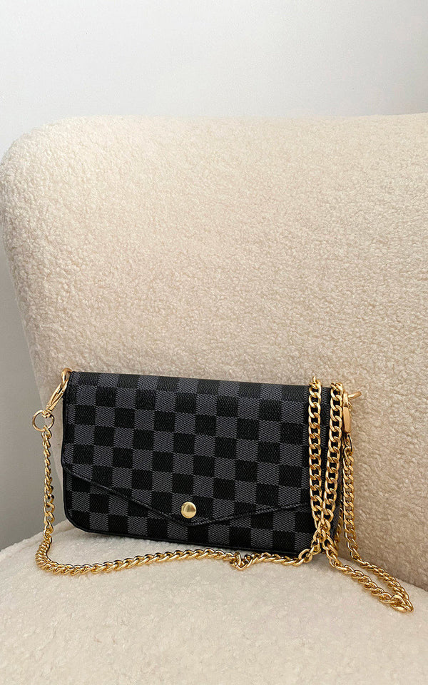 Check Print Clutch Bag with black and gold checkered design, featuring button fastening and detachable gold chain strap, displayed on a white chair.