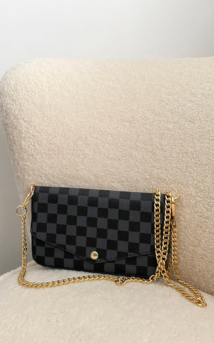 Check Print Clutch Bag with black and gold checkered design, featuring button fastening and detachable gold chain strap, displayed on a white chair.