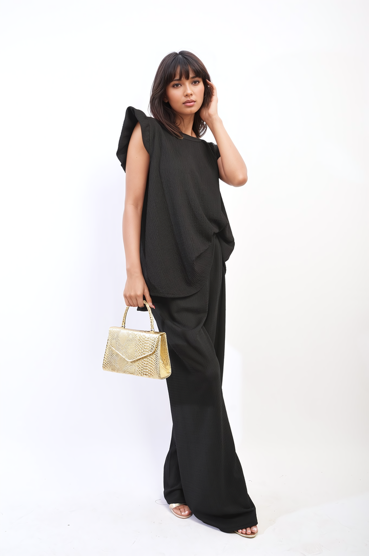 Woman in black holding gold purse, wearing the Ruffle Trim Top and Wide Leg Trouser Co-ord Set, embodying elegance and modern design.