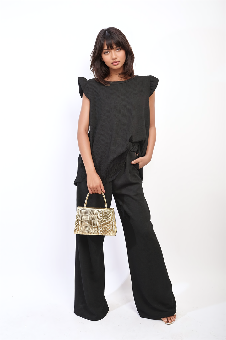 Woman in black outfit holding a gold purse, showcasing the Ruffle Trim Top and Wide Leg Trouser Co-ord Set from Holiday Clothes UK.