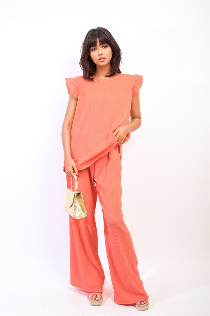 Woman modeling the Ruffle Trim Top and Wide Leg Trouser Co-ord Set, featuring a ruffle-trimmed top and high-waisted trousers, accessorized with a gold purse.