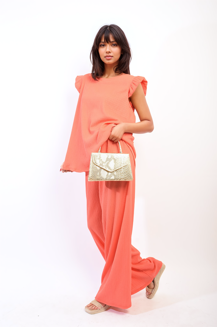 Woman in pink dress holding a gold purse, showcasing the Ruffle Trim Top and Wide Leg Trouser Co-ord Set from Holiday Clothes UK.