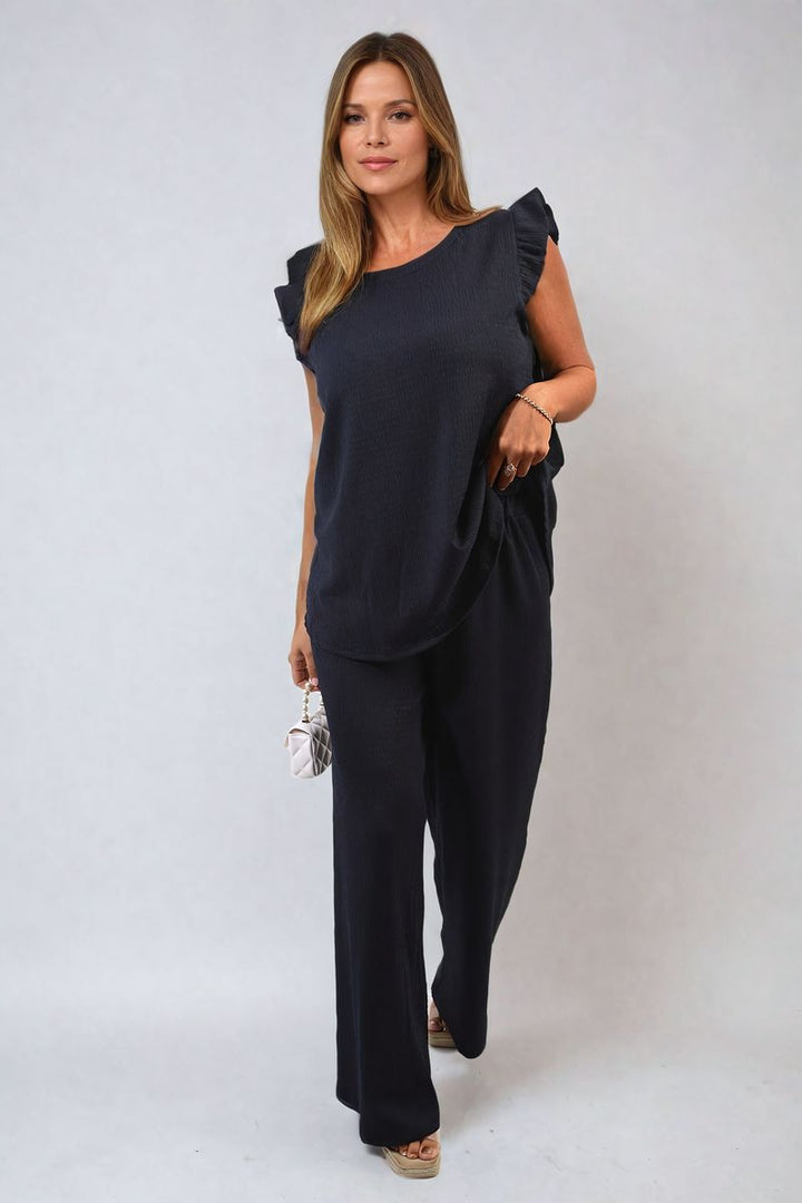 Woman modeling the Ruffle Trim Top and Wide Leg Trouser Co-ord Set, showcasing its elegant ruffle detailing and wide-leg design. Ideal for stylish holiday occasions.