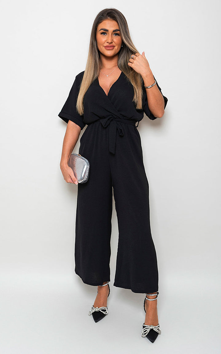 Woman modeling the V Neck Tie Waist Short Sleeve Jumpsuit, showcasing its chic v-neckline and flattering tie waist, perfect for versatile summer styling.