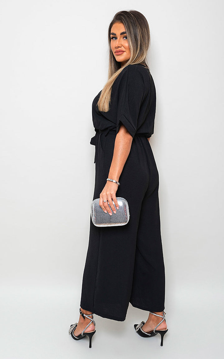 Woman wearing V Neck Tie Waist Short Sleeve Jumpsuit, holding a silver clutch, showcasing summer style and versatility from Holiday Clothes UK.