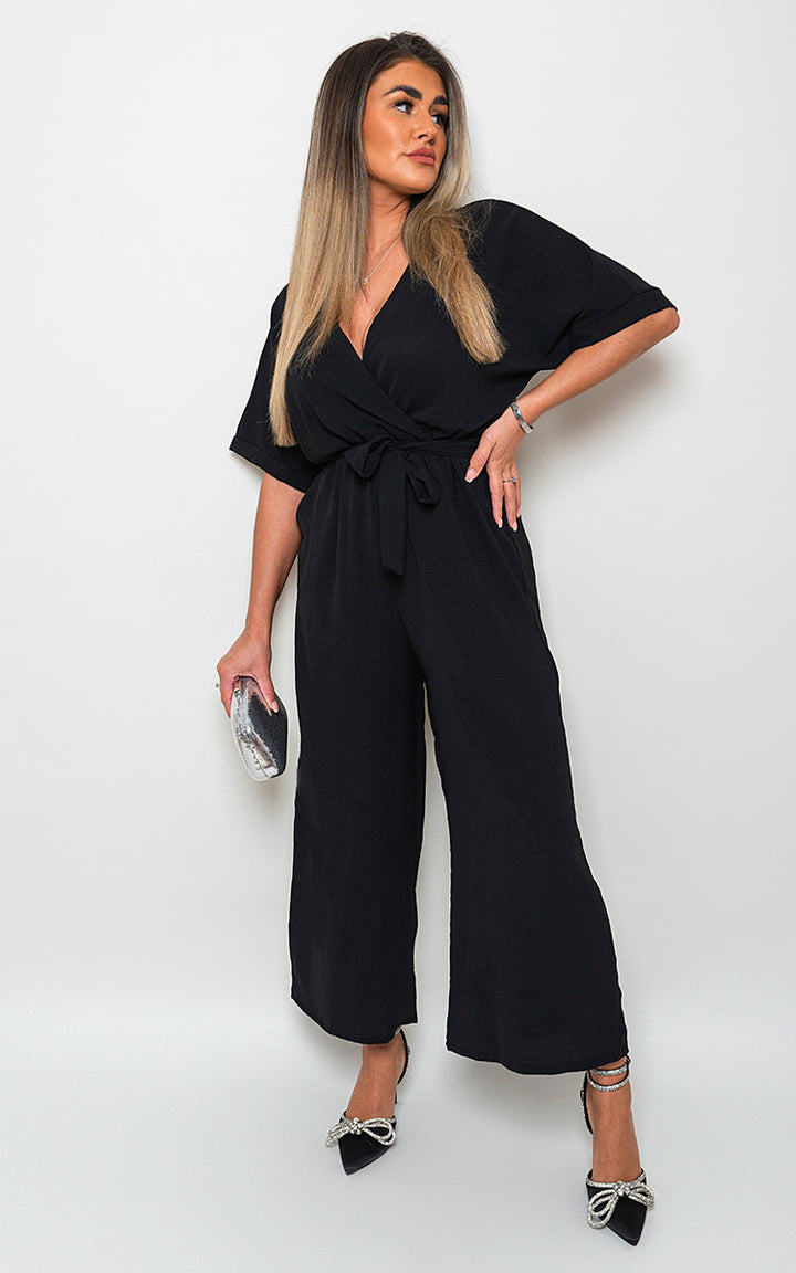 Woman wearing a V Neck Tie Waist Short Sleeve Jumpsuit, showcasing its chic v-neckline and flattering tie waist detail for versatile styling.