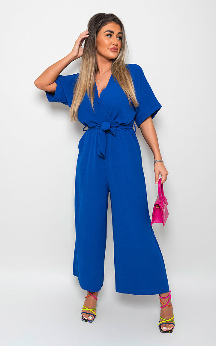 Woman in V Neck Tie Waist Short Sleeve Jumpsuit holding a pink purse, showcasing a stylish and versatile summer wardrobe essential.