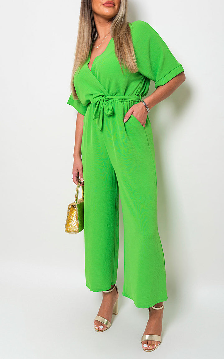 Woman wearing V Neck Tie Waist Short Sleeve Jumpsuit with gold sandals and holding a green and gold purse, perfect for stylish summer outings.