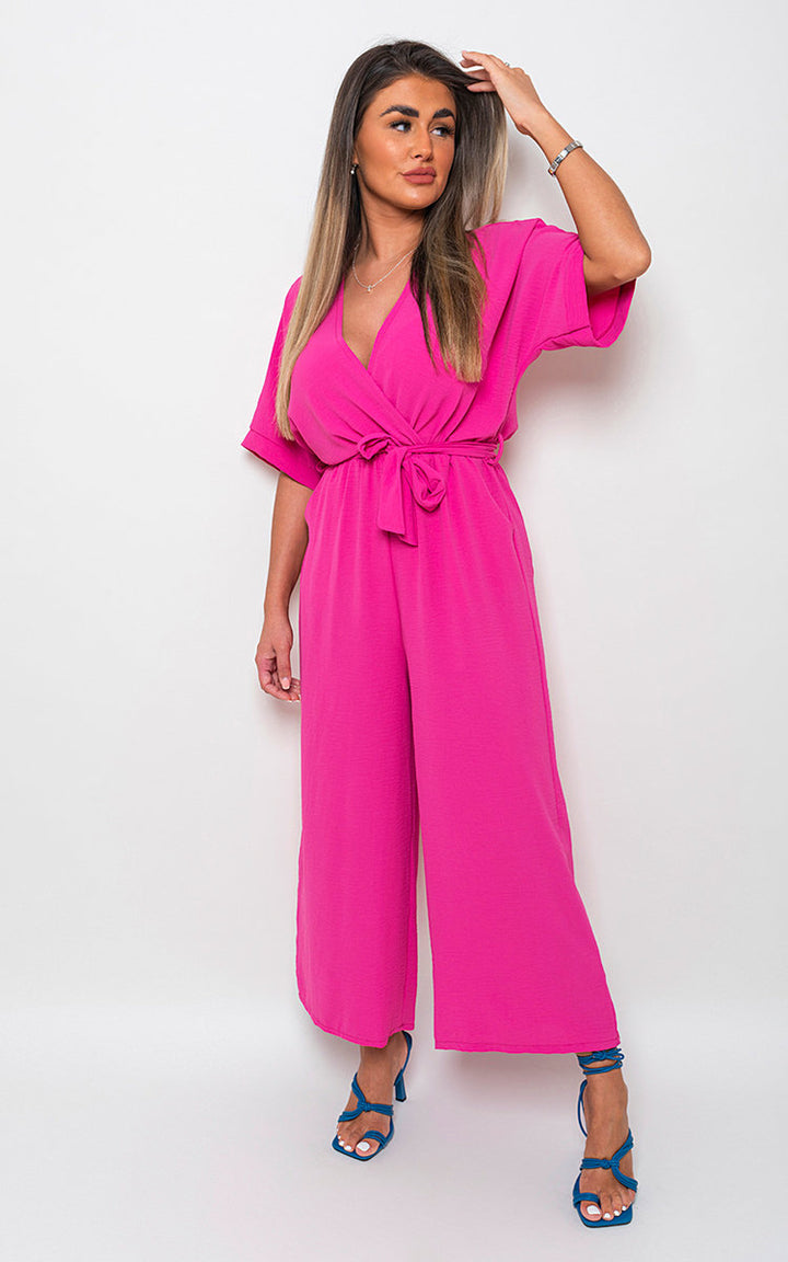 Woman modeling the V Neck Tie Waist Short Sleeve Jumpsuit, showcasing its chic v-neckline and flattering tie waist detail, perfect for versatile summer styling.