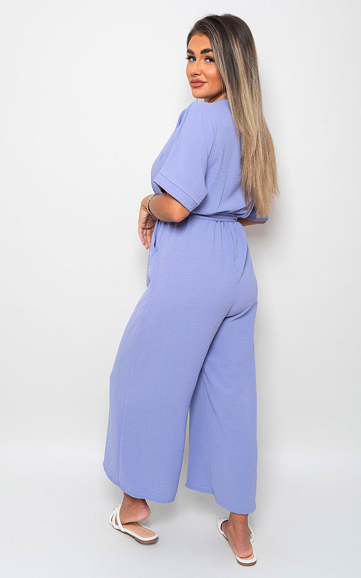 Woman wearing V Neck Tie Waist Short Sleeve Jumpsuit, showcasing its chic v-neckline and flattering tie waist, perfect for versatile summer styling.