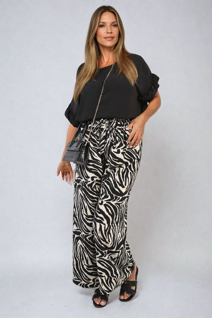 Woman wearing stylish zebra-striped wide leg trousers, paired with a black shirt, showcasing a bold fashion statement. Ideal for casual or chic occasions.