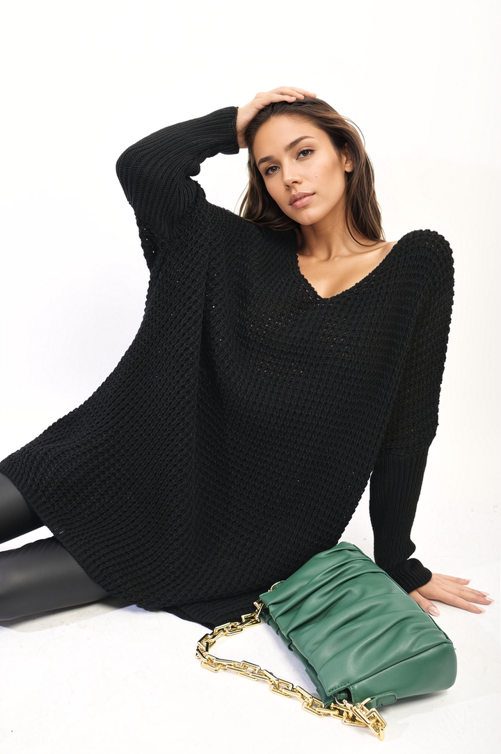 Woman wearing an oversized chunky knitted jumper, sitting and posing with a green purse, highlighting the cozy and stylish design of the Rebecca Jumper.