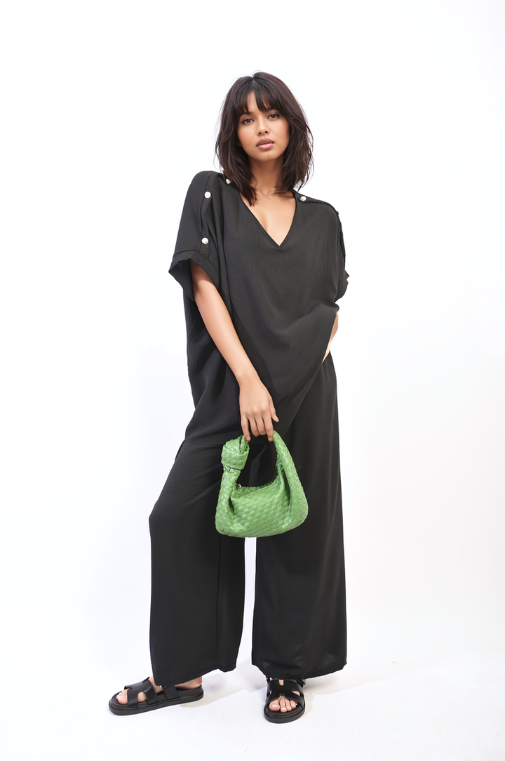 Woman in black outfit holding a green purse, showcasing the Button Detail V Neck Loose Top and Wide Leg Trouser Co-ord Set from Holiday Clothes UK.