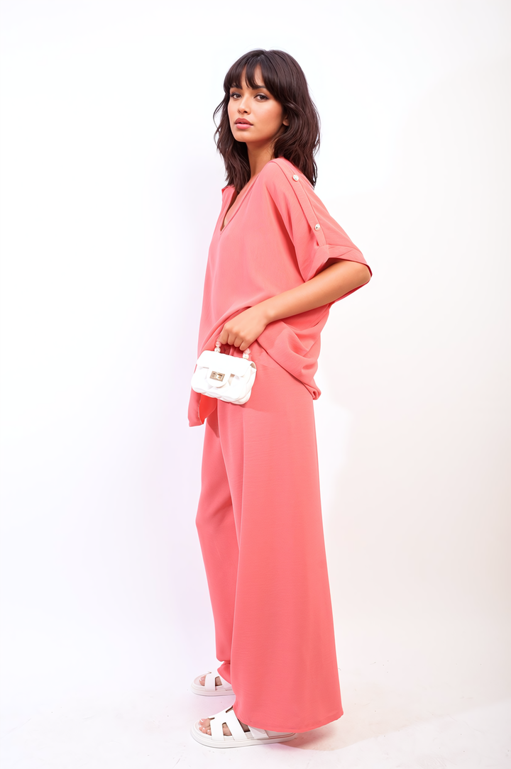 Woman wearing Riley Button Detail V Neck Loose Top and Wide Leg Trouser Co-ord Set, holding a white purse, showcasing a chic, comfortable outfit.