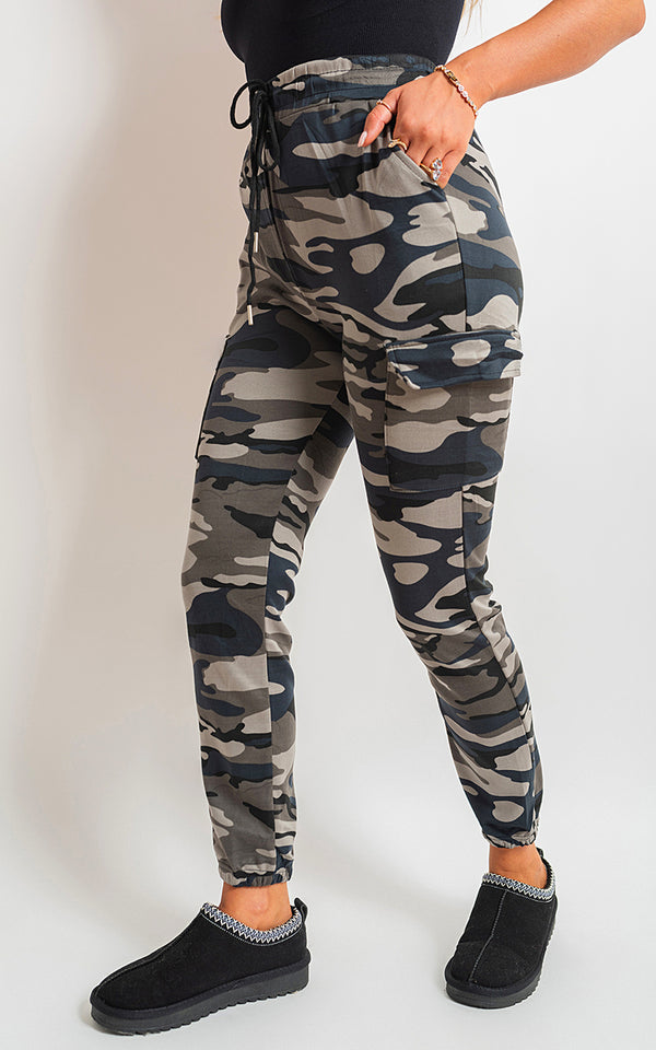 Woman wearing Robyn Camo Print Tie Cargo Trousers, showcasing adjustable tie waist and functional pockets, paired with black footwear for a stylish, casual look.