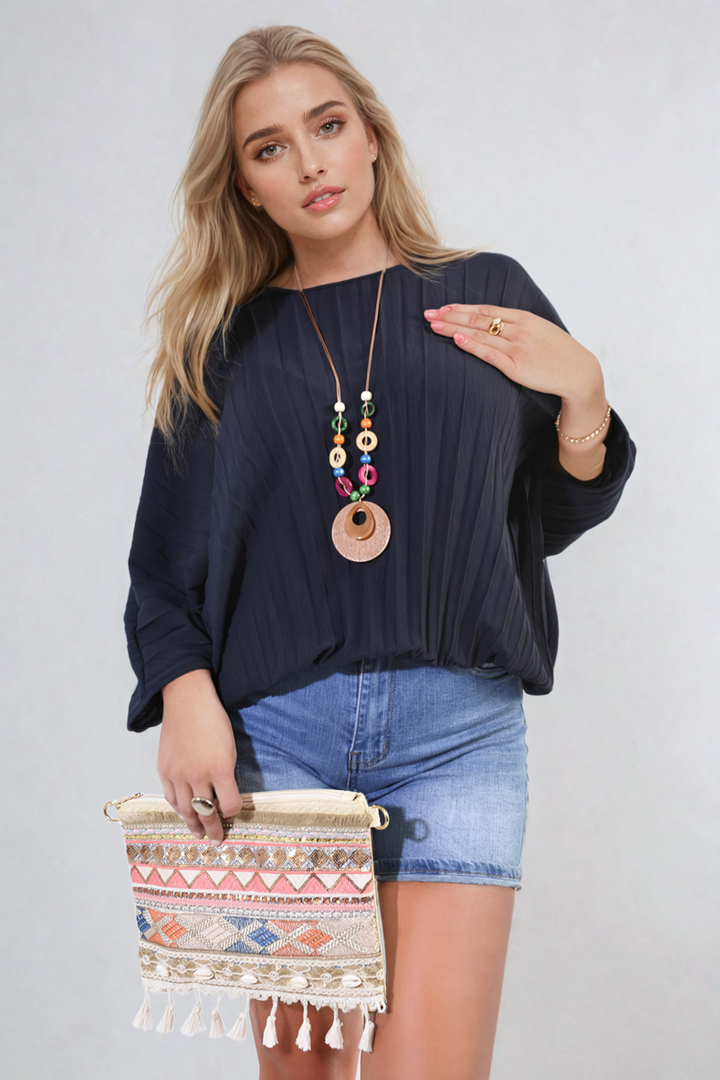 Woman wearing Rowena Batwing Oversized Pleated Top, holding a colorful purse, showcasing the top's dramatic batwing sleeves and pleated detailing.