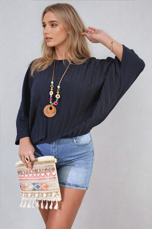 Woman wearing the Rowena Batwing Oversized Pleated Top, showcasing its dramatic batwing sleeves and modern pleated design, paired with a stylish handbag.