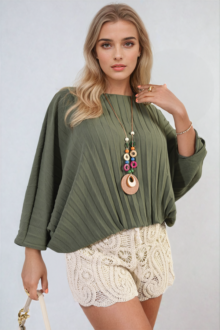 Woman wearing a Rowena Batwing Oversized Pleated Top, showcasing its dramatic batwing sleeves and modern pleated detailing. Perfect for stylish holiday or everyday wear.