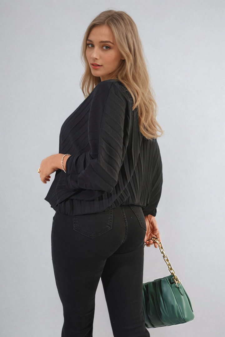 Woman models the Batwing Oversized Pleated Top with batwing sleeves, paired with black jeans and accessorized with a green purse featuring a gold chain.