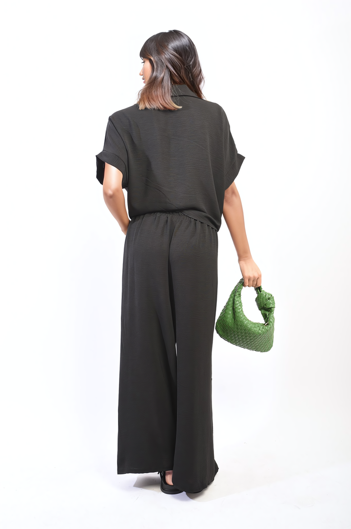 Woman in black outfit holding a green purse, wearing the Ruby Tie Front Top and Wide Leg Pants Co-ord Set, showcasing stylish comfort.