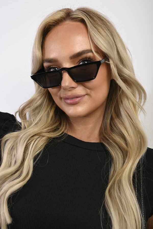 Woman wearing Rylan Skinny Trapezoid Sunglasses, showcasing sleek, modern eyewear design with UV protection, perfect for stylish holiday and everyday fashion.