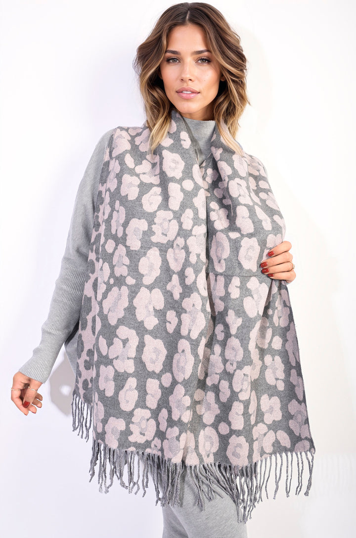 Woman wearing the Saira Animal Print Scarf with Tassel, showcasing its bold print and tassels, adding a fashionable touch to her grey sweater.