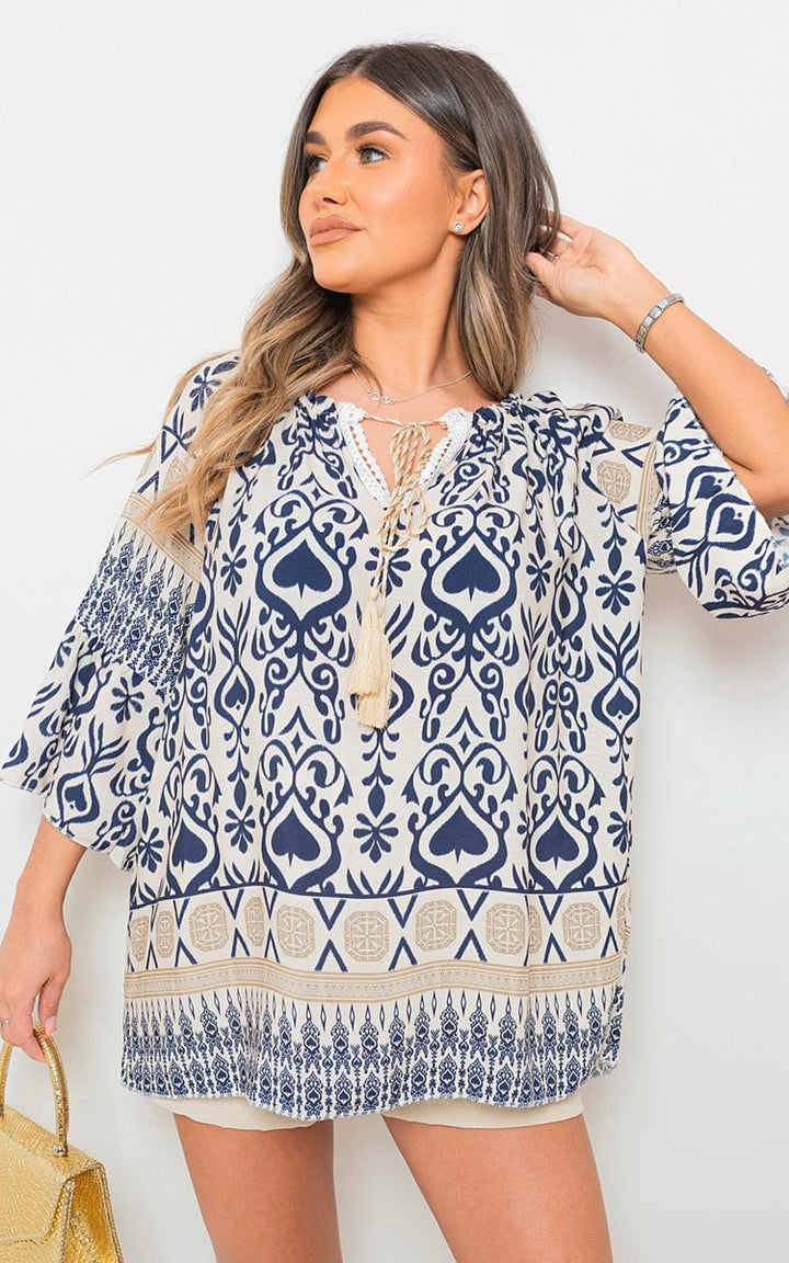 Woman in a blue and white dress showcasing the Boho Printed Tassel Tie Neck Long Sleeve Loose Top, featuring a tassel tie neck and intricate patterns.