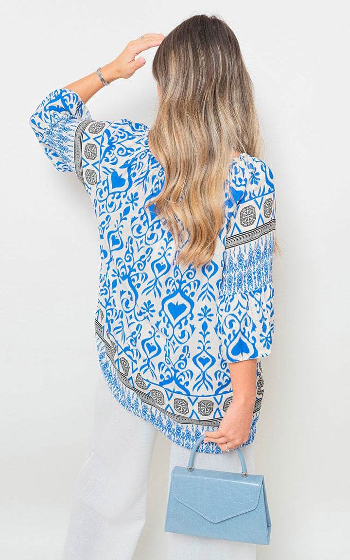 Woman wearing Boho Printed Tassel Tie Neck Long Sleeve Loose Top, holding a blue purse, showcasing the top's intricate patterns and tassel detail.