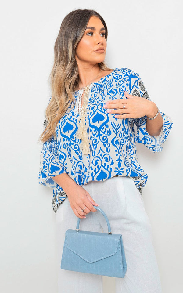 Woman wearing Boho Printed Tassel Tie Neck Long Sleeve Loose Top, holding a blue purse, showcasing the top's intricate boho print and tassel details.