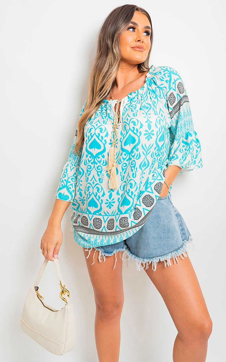 Boho Printed Tassel Tie Neck Long Sleeve Loose Top worn by a woman, featuring a tassel detail and vibrant bohemian print, complemented by a white purse.