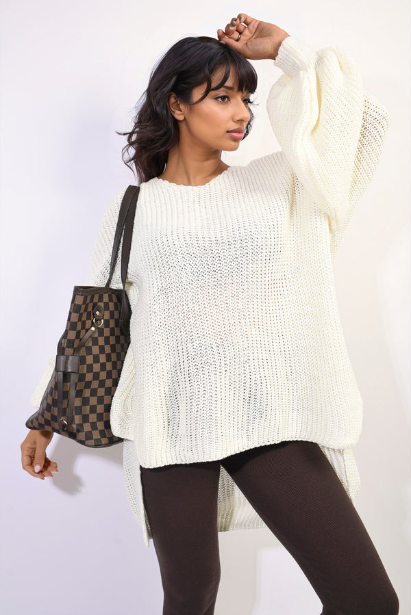 Woman in a white sweater wearing an oversized long back knitted mini dress, showcasing its stylish, relaxed fit and intricate knit pattern.