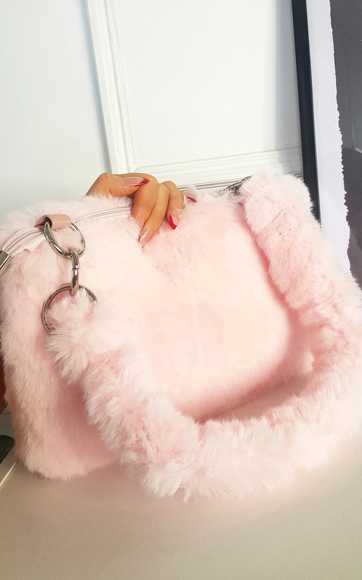 Hand holding a pink Faux Fur Shoulder Bag with Fluffy Strap, showcasing its soft texture and metal accents, ideal for versatile use.