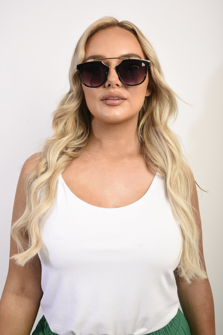 Woman wearing Brow-Bar Cat Eye Sunglasses with a white tank top, showcasing the sunglasses' stylish cat eye shape and brow-bar detail. Perfect for chic holiday looks.