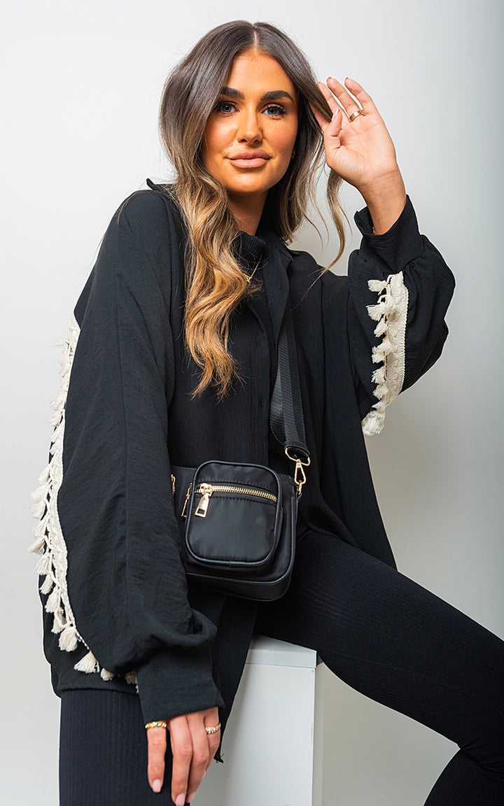 Woman wearing an oversized long sleeve tassel trim top, featuring boho-inspired design and tassel accents, paired with a black handbag.