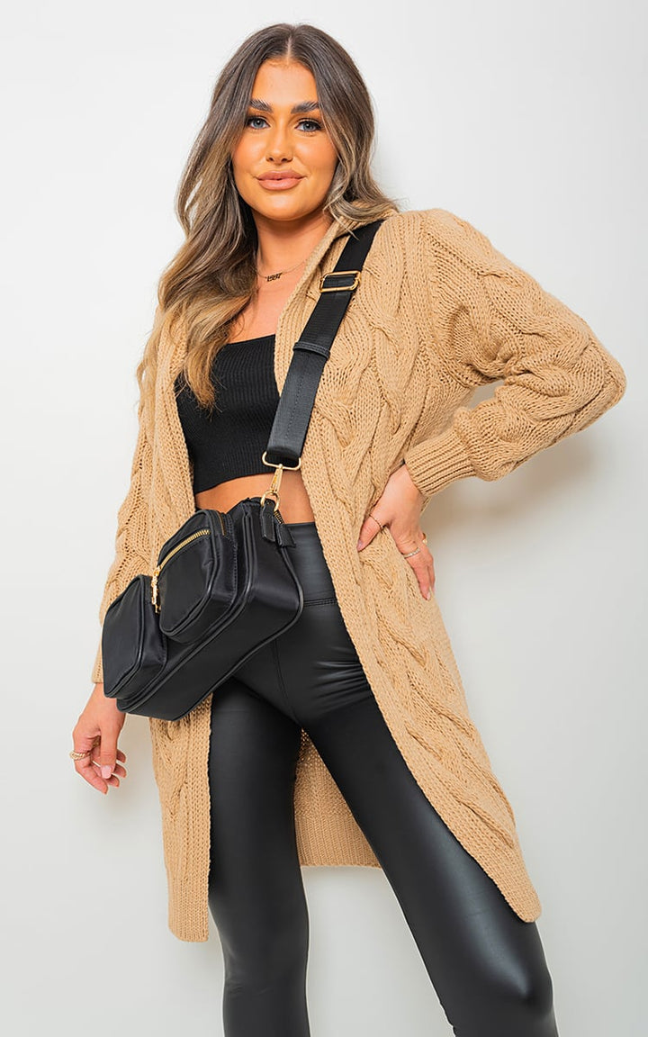 Woman wearing a Chunky Cable Knitted Oversized Longline Hooded Cardigan, posing with a black purse, highlighting the cardigan's cozy, layered style.