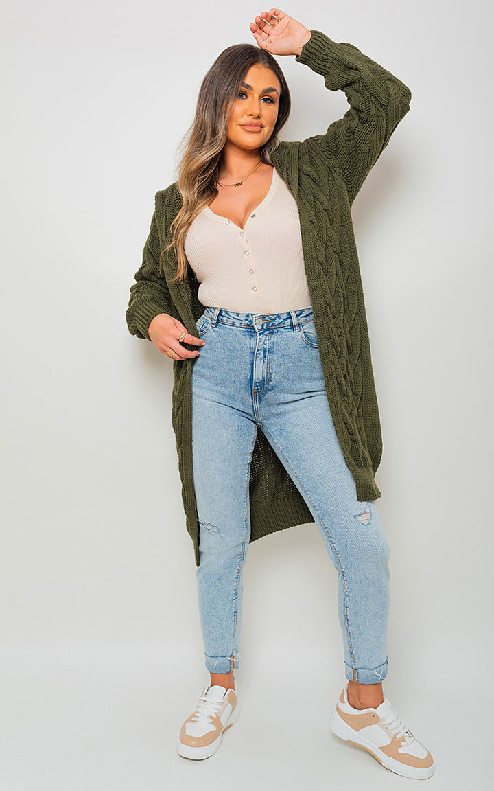 Woman wearing Chunky Cable Knitted Oversized Longline Hooded Cardigan, posing casually. The cardigan's cozy, layered design highlights its stylish and comfortable appeal.