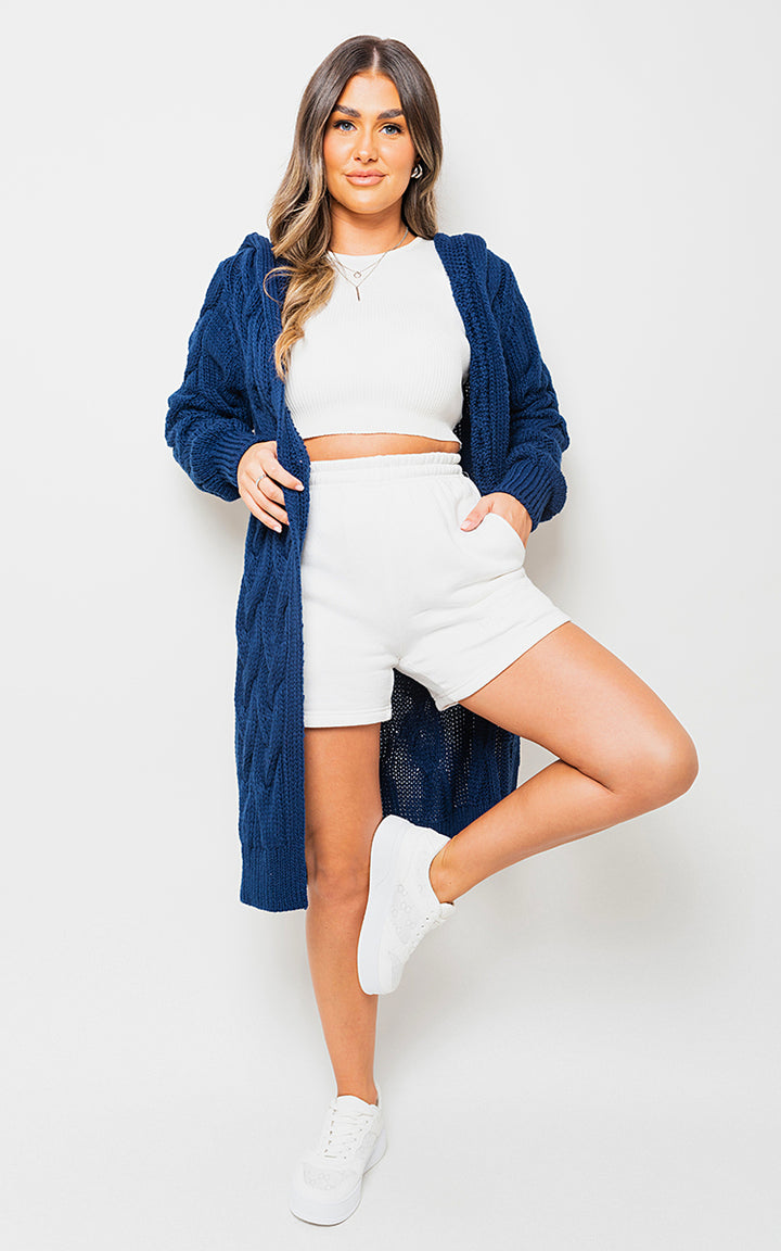 Woman wearing Chunky Cable Knitted Oversized Longline Hooded Cardigan, posing casually. Ideal for layering and cozy days, representing 'Holiday Clothes UK' style.