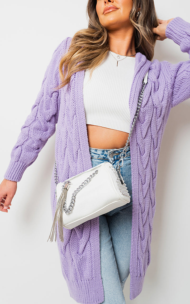 Woman wearing Chunky Cable Knitted Oversized Longline Hooded Cardigan and holding a white purse, showcasing cozy fashion from Holiday Clothes UK.